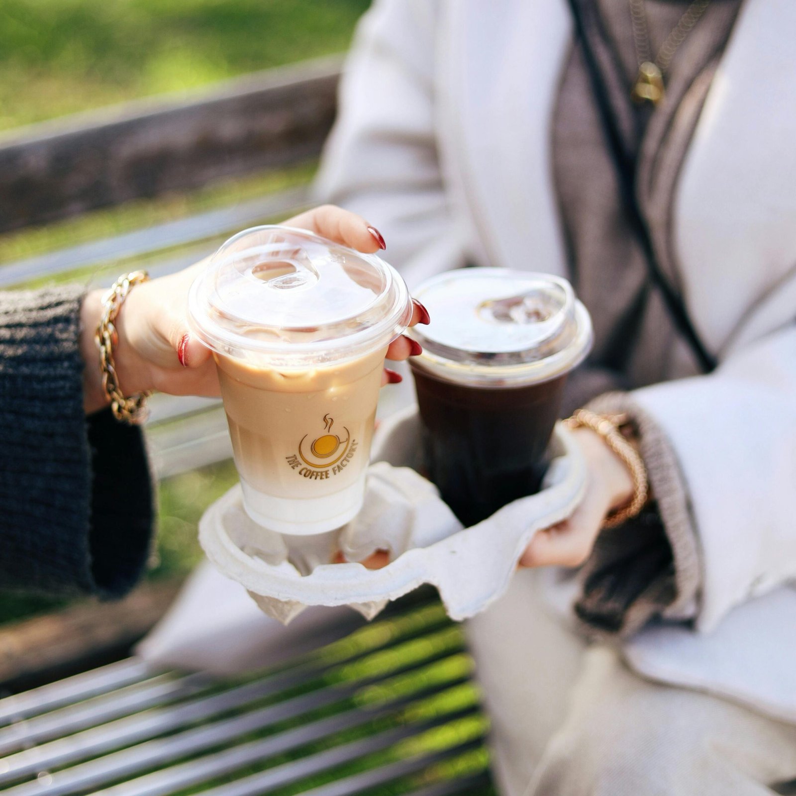 Two women holding coffee cups in a park setting, enjoying a casual outdoor moment.
